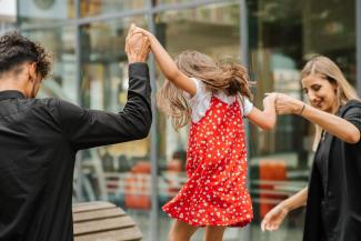 Parents holding their child's hands. The child is jumping